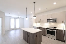 Kitchen with a quartz countertops island facing the living area with double glass door leading to the patio. 