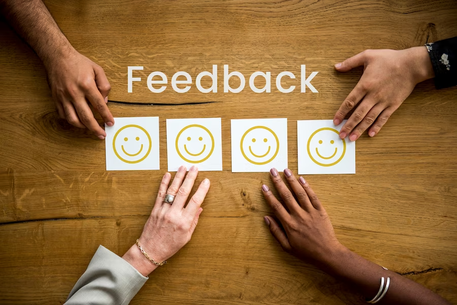 Four hands on a table with the word 'feedback' written on it, along with smiley faces