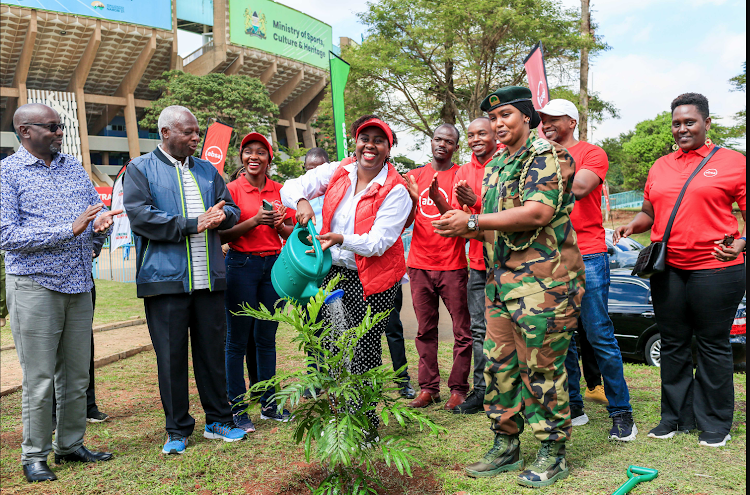 Absa bank's chief marketing officer Carolyne Kendi (centre) waters a tree during tree planting session at Kasarani Stadium