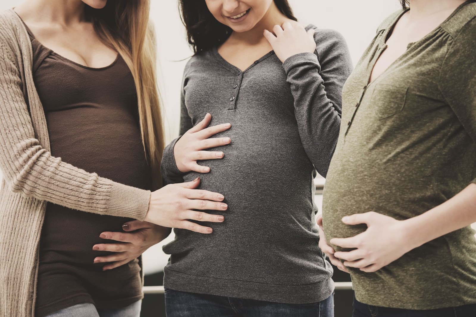 Três mulheres grávidas tocando nas barrigas e interagindo.