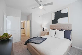 Model unit bedroom with light colored walls, neutral colored carpet with a walk in closet and attached bathroom