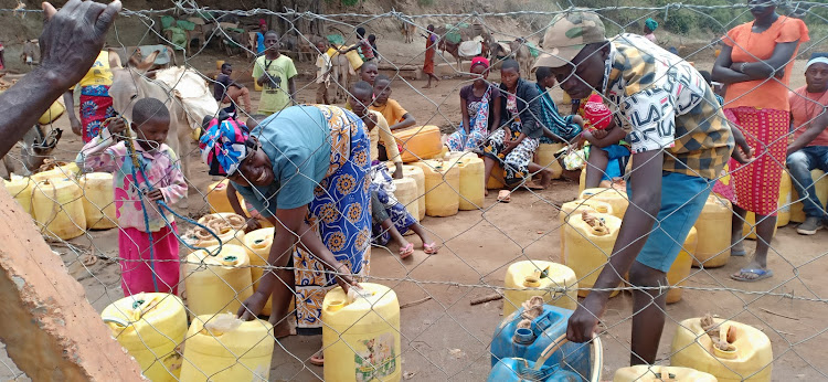 Residents queue for their turn to get water at a water point bedsides the Mathima earth dam in Kitui South on Thursday.