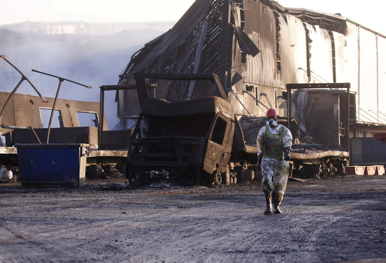 A member of a hazardous waste cleanup crew walks to clean up a warehouse burnt during the looting in Durban on July 17.