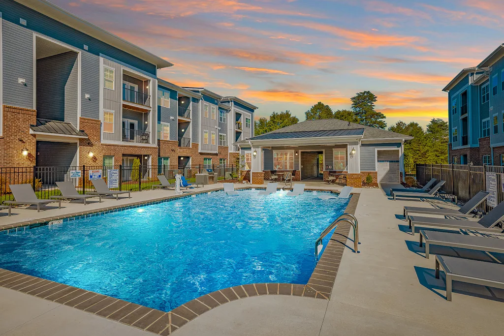 Grand Oaks' fenced-in swimming pool at dusk with a sundeck featuring lounge chairs and buildings in the background