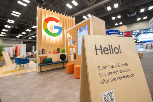 Photo of a Google booth with a sign up close that reads 'Hello!' Scan the QR code to connect with us after the conference.