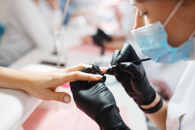 Mestre em luvas trabalha com unhas, procedimento de manicure em salão de beleza.