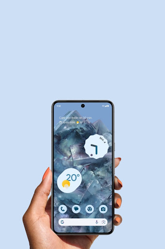 Una mano sostiene un Pixel 8 Pro en color celeste. La pantalla de inicio del teléfono brilla con luz propia con su nuevo diseño. 