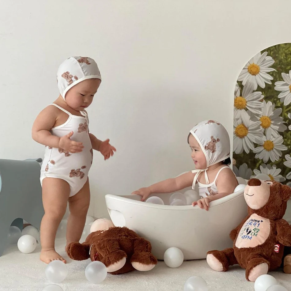 Maiô infantil fofo com estampa de desenho animado e chapéu, ideal para natação e brincadeiras na praia com proteção solar.