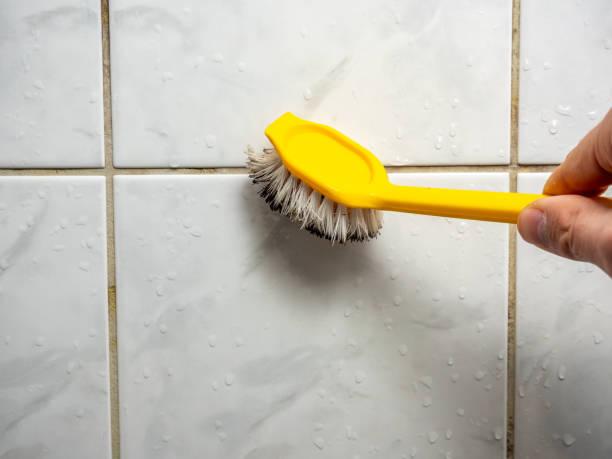 WeServe man cleaning the mold from the tiles of the bathroom