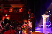 A woman lights a candle on stage at the memorial service for jazz musician Gloria Bosman.