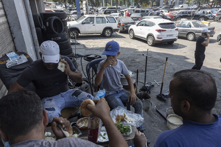 A child shares breakfast with his colleagues who are using burger buns in addition of traditional bread due to a recent closure of bakeries due to fuel shortages, at a petrol station in Beirut, Lebanon, on August 14, 2021.