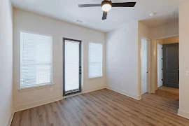 Living room with wood plank flooring, white walls and trim, patio door with blinds, and two windows with blinds