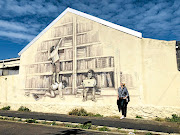 Writer Allison Foat gazes on Justin Nomad's mural on Tennyson Street. Titled 'The Library', it shows the contrasting ways of learning from the past to the present.  