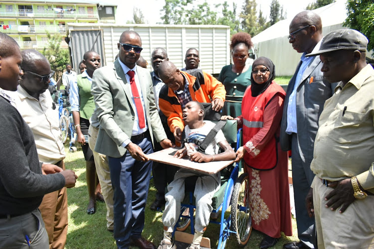 Dr. Andrew Wamalwa (in specks) handing over a wheelchair to a beneficiary.