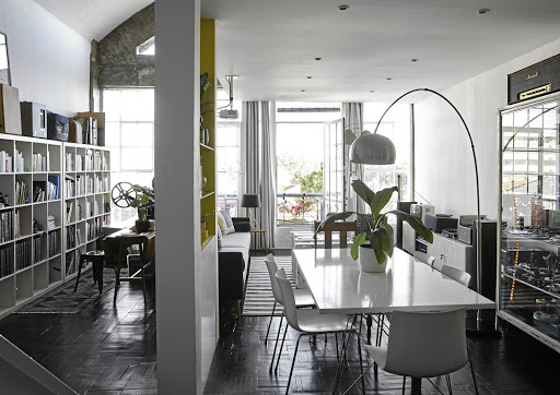 The open-plan living space is sliced in two by a wall display: on one side is a collection of books, guitars and projectors, and on the other the homeowner's modernist-style design pieces, such as the Arco-style lamp and Catifa chairs.