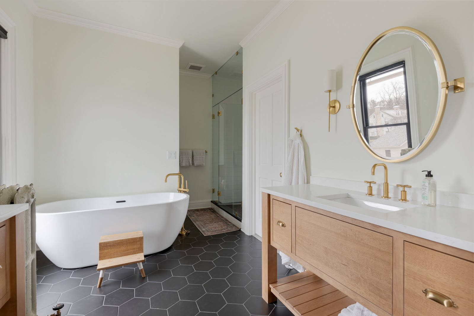 Primary-bath-remodel-with-large-soaker-tub-honeycomb-charcoal-tile-flooring-white-walls-and-natural-maple-vanity-with-quartz-countertop-and-gold-accents