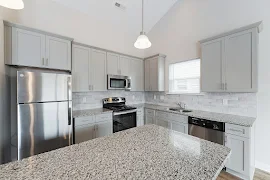 Kitchen with speckled stone countertops, island, gray shaker cabinets, tile backsplash, and stainless steel appliances