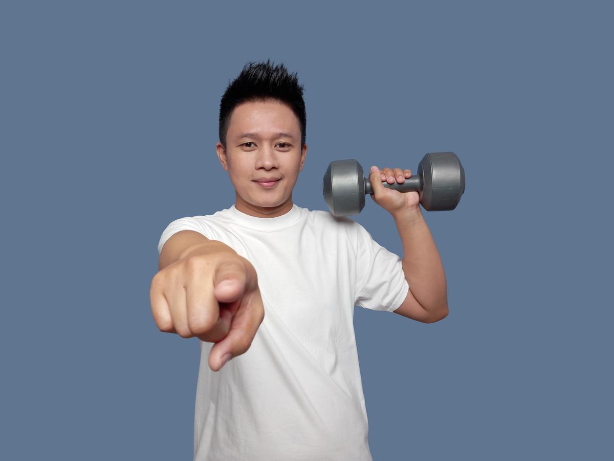 A person holding a dumbbell pointing at the camera
Description automatically generated