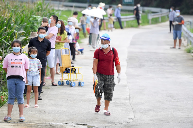 A worker disinfects next to villagers lining up by a corn field for nucleic acid testing at Baiyangping village following the coronavirus disease (Covid-19) outbreak in Zhangjiajie, Hunan province, China. August 12, 2021.