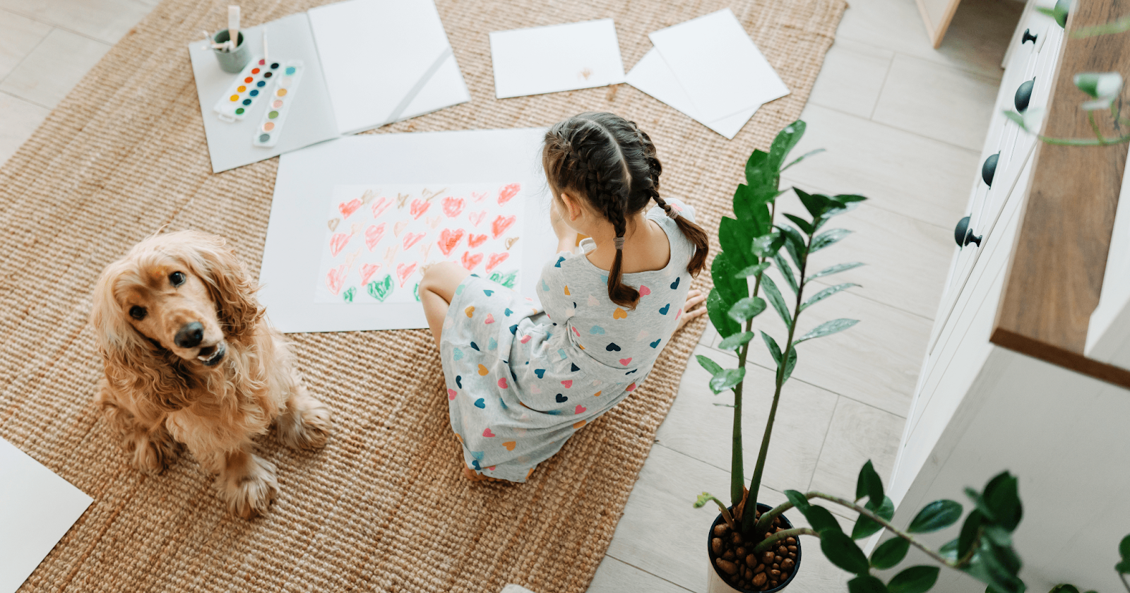 Little girl on floor painting with Cocker Spaniel sitting beside her