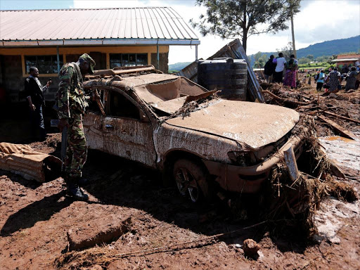 A military officer assesses a damaged car after a dam burst, which unleashed water at nearby homes, in Solio town near Nakuru, Kenya May 10, 2018. /REUTERS