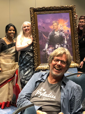 Guido van Rossum standing in front of a painting depicting him. Displayed by PyLadies Organizers.