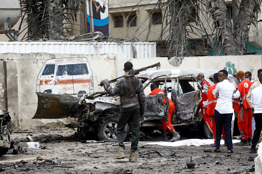 A police officer keeps watch as Red Crescent workers remove the body of a victim at the scene of a suicide car bomb explosion near the president's residence, in Mogadishu, Somalia, September 25, 2021.