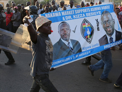 Supporters of opposition leader Kizza Besigye walk past riot police while holding a banner in Kampala, Uganda, February 16, 2016. Photo/REUTERS