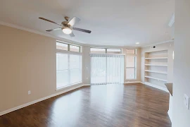 Open living room with wood flooring, large windows, built in shelf, and a ceiling fan