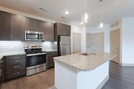 Kitchen with dark cabinets, stainless steel appliances, granite countertop, island with sink & two pendant lights, wood floors