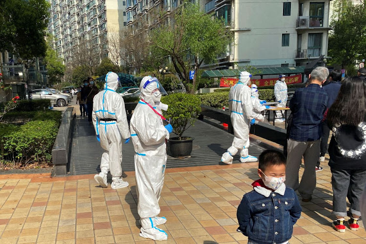 Medical workers in protective suits stand next to a line of residents waiting to take nucleic acid test at a locked down residential area, following the coronavirus disease (Covid-19) outbreak in Shanghai, China April 7, 2022.