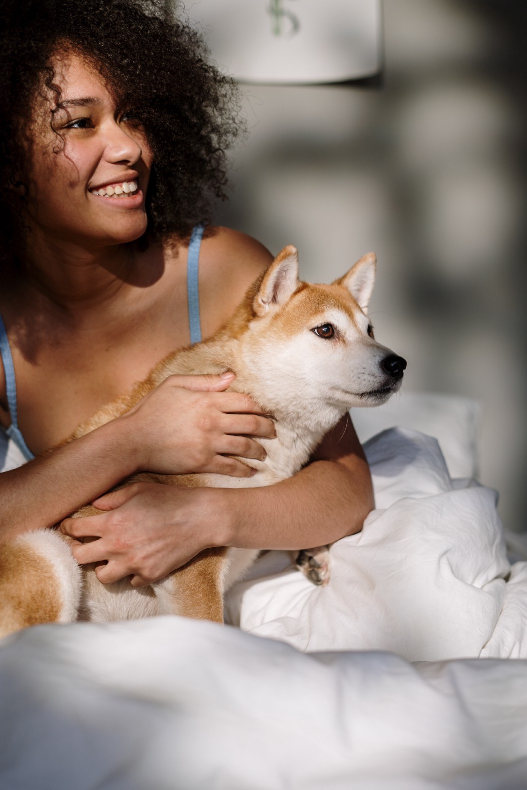 How to wake up early: smiling girl is holding her dog in bed in early morning