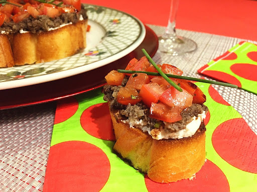 A slice of bread with cheese, mushroom paste and tomato pieces garnished with chives.