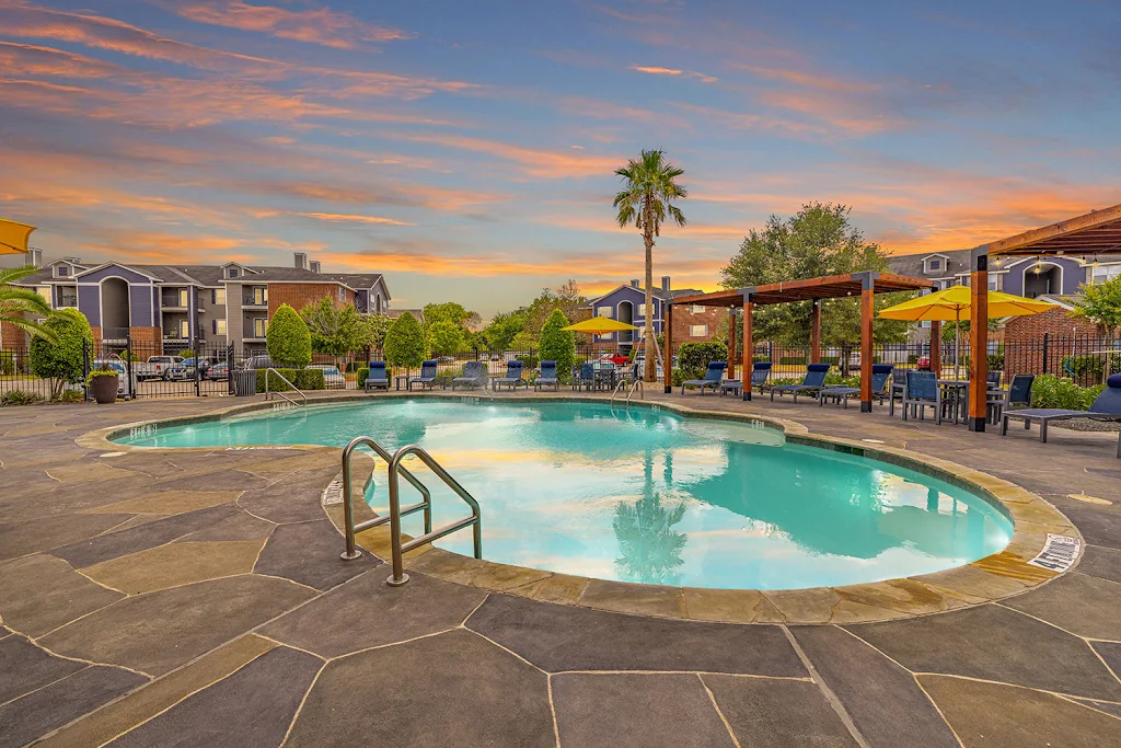 Grand Palms' swimming pool at dusk with large sundeck featuring wood pergolas with string lights and blue lounge chairs