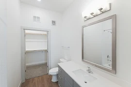 Bathroom with large gray vanity with white countertop, mirror, tall ceiling, access to walk-in closet, wood inspired flooring