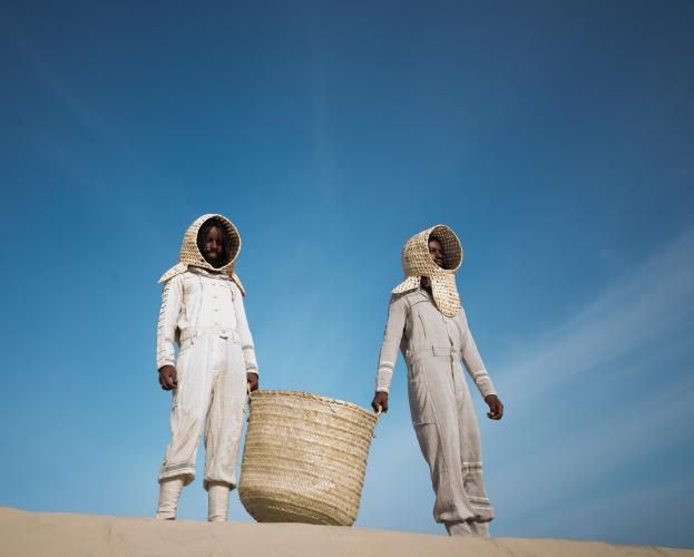 Each wears a space suit that’s made of cotton and cuffed at the ankles. Some are hooded; others gaze out through the portal of their basketweave space helmets.