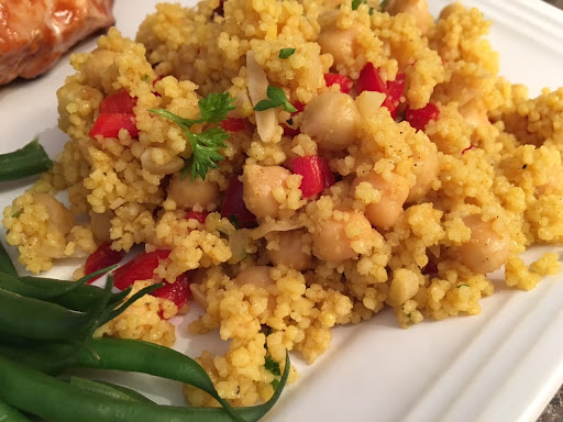 A couscous salad served on a white plate next to green beans.