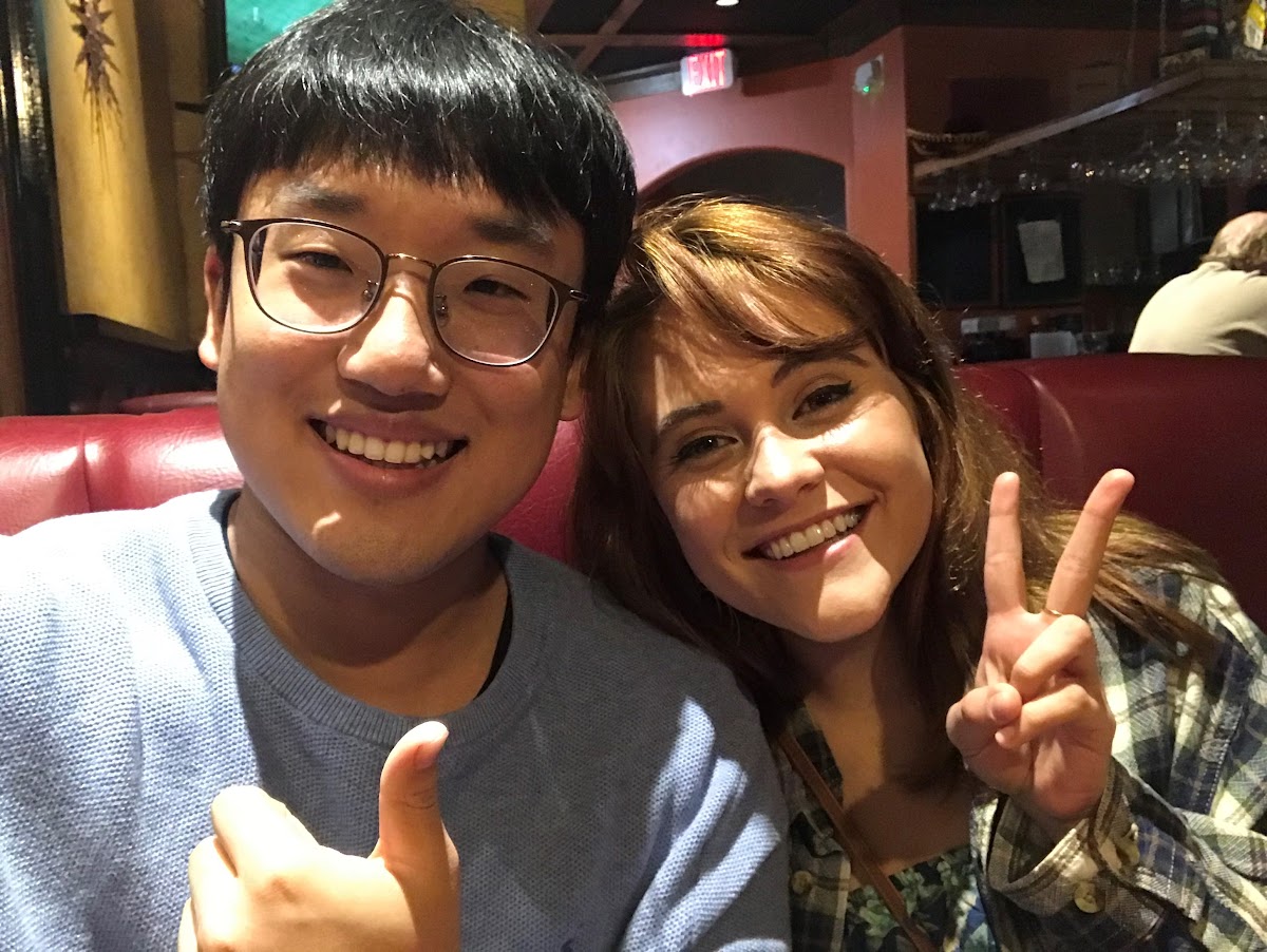 Close up of two buddies with wide smiles flashing a peace sign and thumbs up seated in a booth