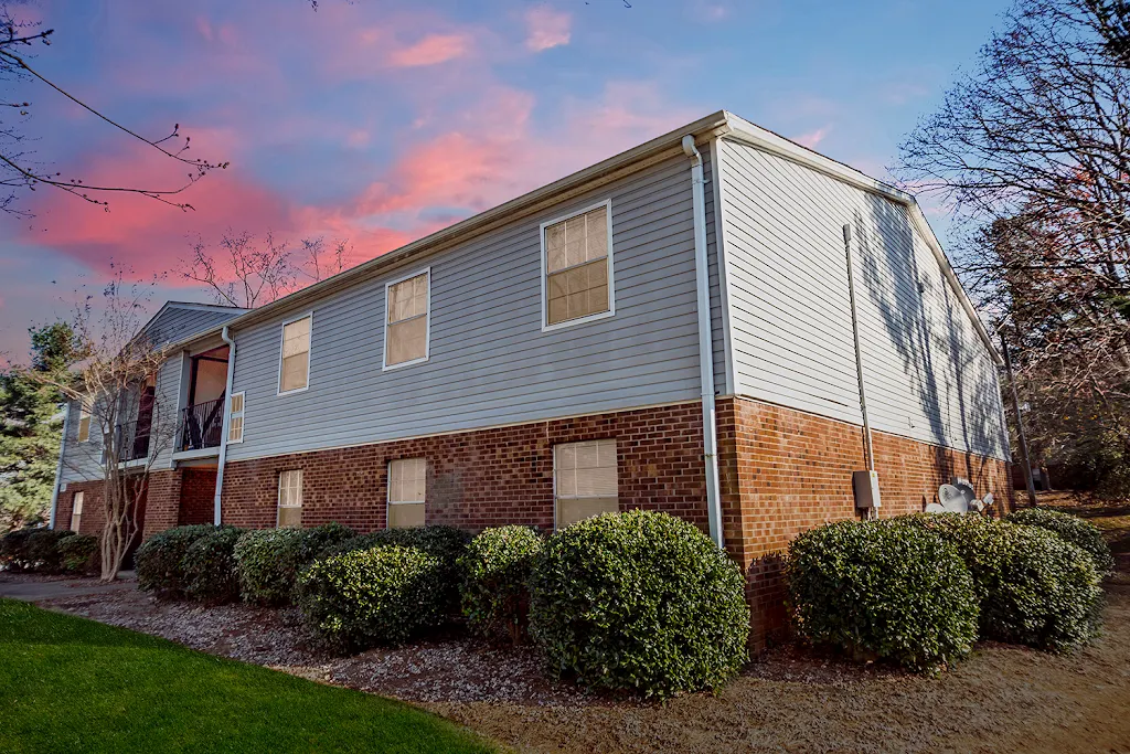 Colonial Apartments building exterior at dusk.  Upper siding.  Lower brick. Landscaped bushes. 