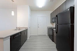 Modern apartment kitchen with black appliances, dark wood cabinets, and light flooring.