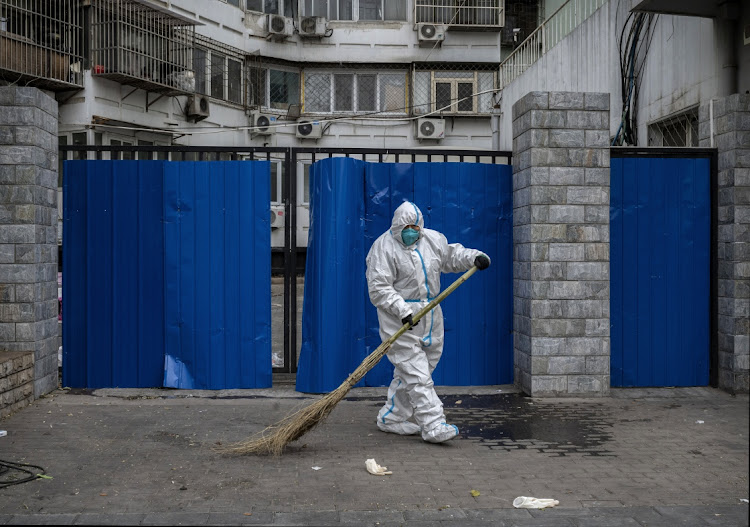 An epidemic control worker wears PPE to prevent the spread of Covid-19 as he sweeps while cleaning an area outside a barrier fence in an area with communities in lockdown on December 2 2022 in Beijing, China. Picture: GETTY IMAGES/KEVIN FRAYER