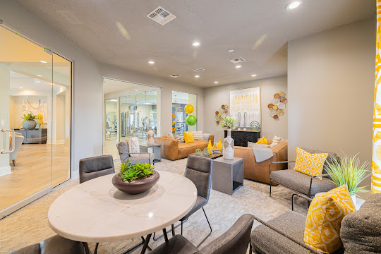 Clubhouse lounge area with couches, chairs, a round table with four gray chairs, and contemporary decor