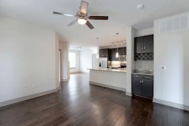 Living room with dark wood-inspired floors, neutral trim & light walls with an inset cabinet with counter & upper wine rack.