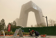 Construction workers are seen in front of the CCTV headquarters shrouded in dust as the city is hit by a sandstorm, in Beijing, China, on March 28 2021. 