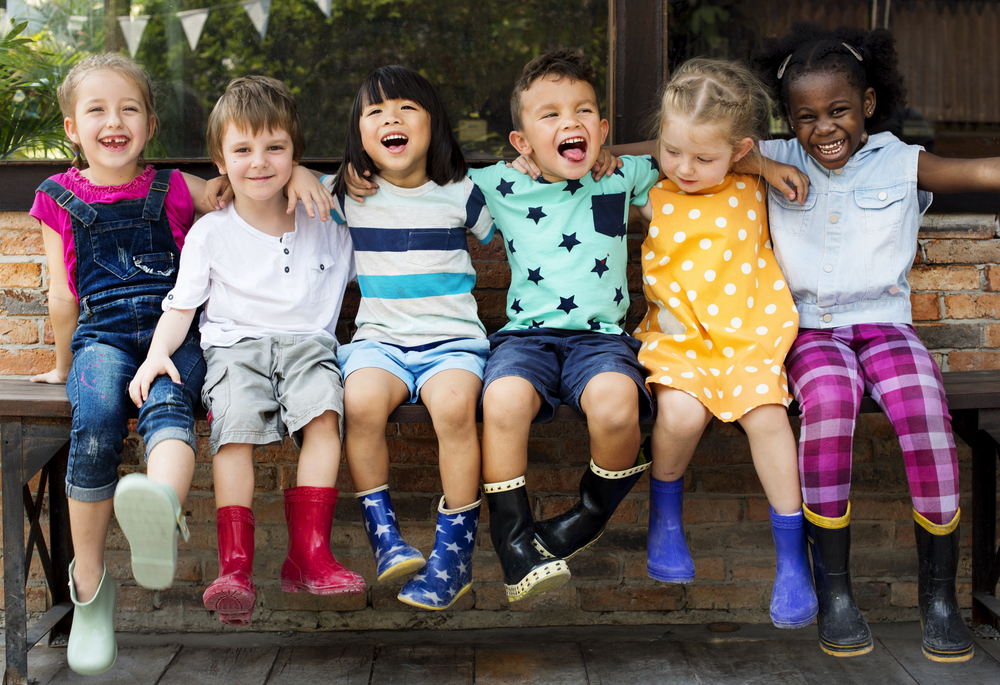 Group of kids sitting on a bench with arms around each other, smiling and laughing