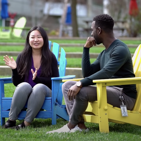 In a grassy outdoor setting, two people sit across from each other, smiling and engaged in conversation