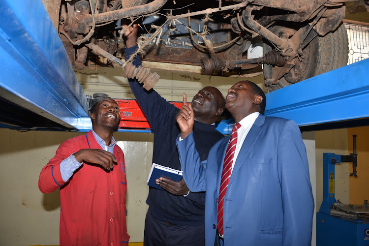 Calvin Cheruiyot (L), the garage manager, Fredrick Obiero (C), chief principal of Rift Valley Technical Training Institution (RVTTI) inspect underside of the 1970 Volkswagen pick up.