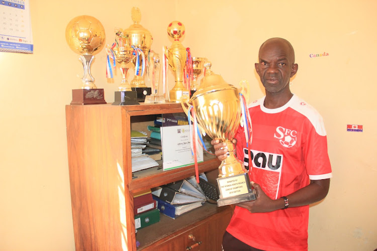 MYRC’s Anthony Obala holds one of 31 trophies won by his team during an exclusive interview with KNA recently in his office, by Rolex Omondi.