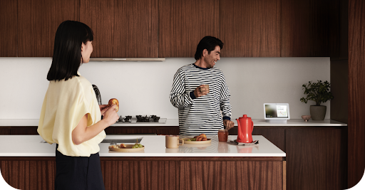 An image of two people in a kitchen using the Google Home app on their Nest Hub device