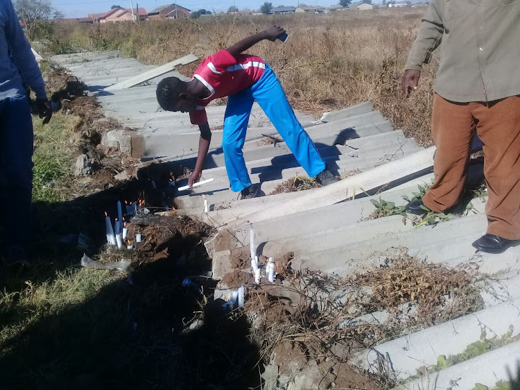 Community members lights a candle at the place where the girls bodies were found.